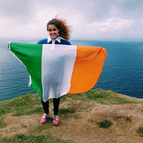 A student poses on a cliff with the Irish flag